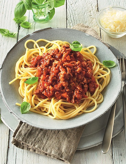 Spaghetti mit Geflügel-Bolognese auf einem Teller serviert mit Basilikum dekoriert