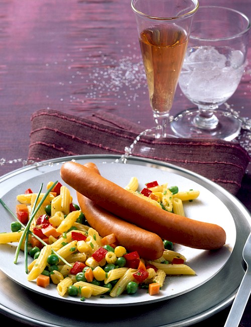 Geflügel-Wiener mit Gemüse-Nudelsalat auf einem Teller serviert